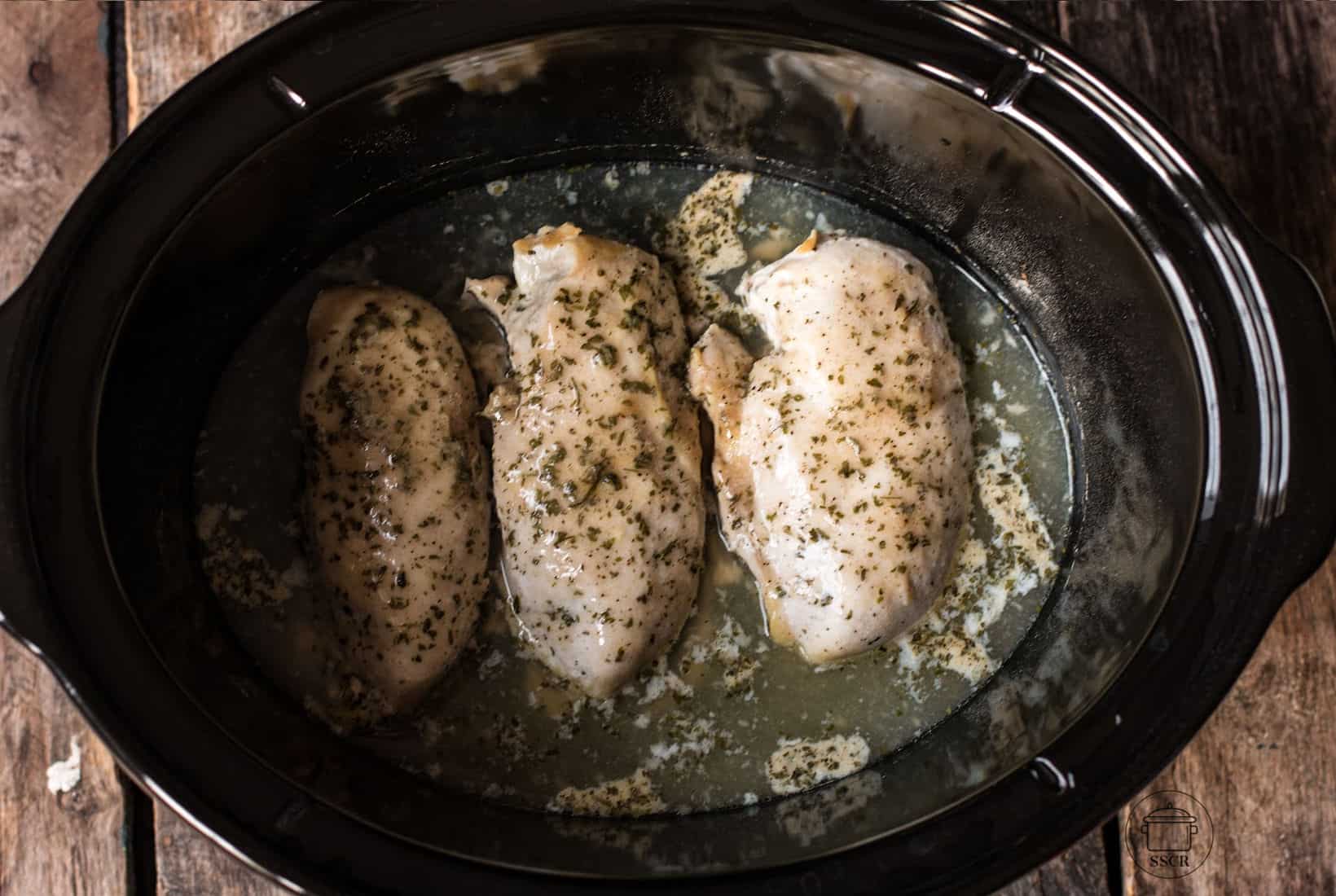 3 cooked chicken breasts with ranch dressing powder seasoing in a slow cooker.