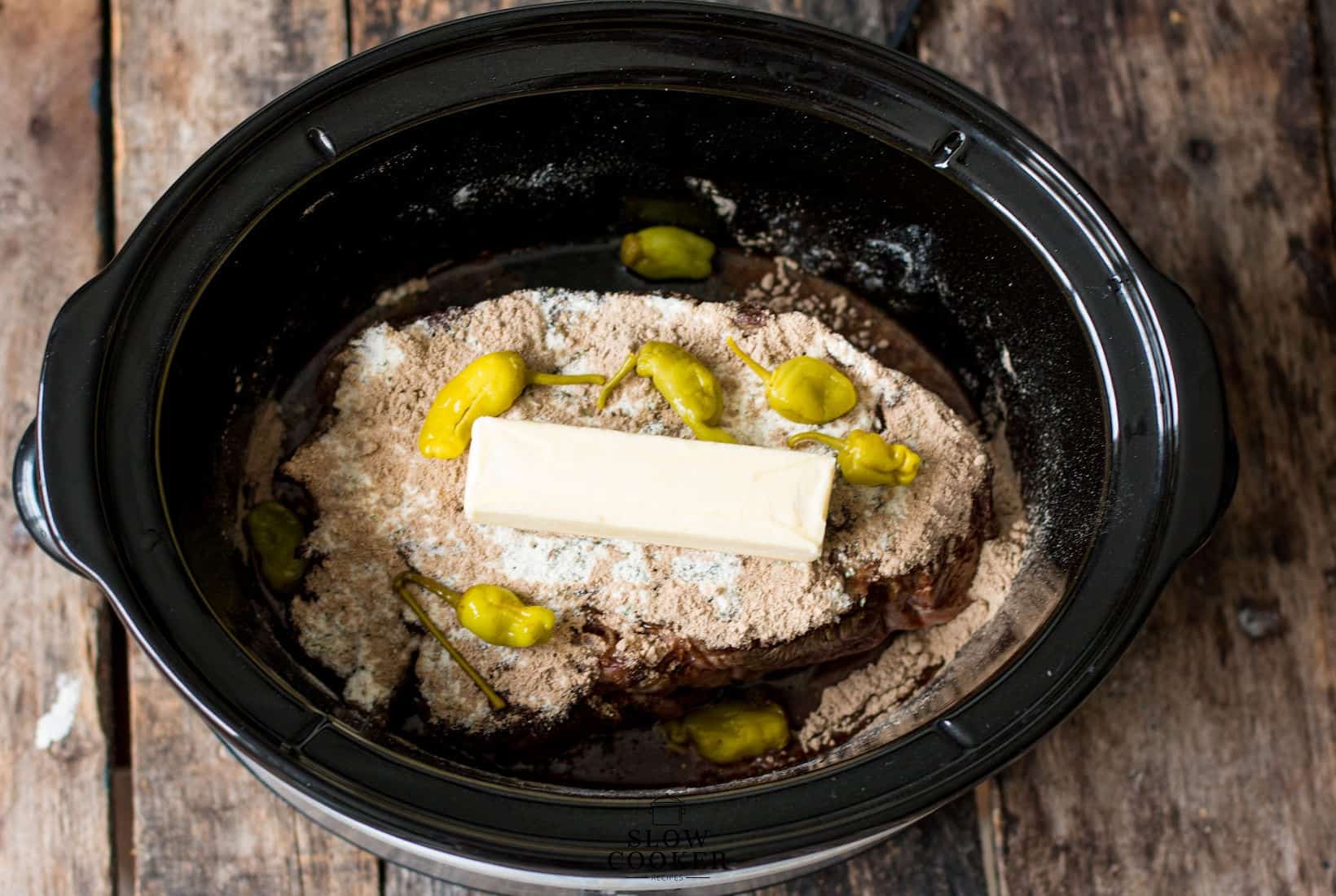 butter, au jus, peperonchini, ranch dressing on top of the beef in a slow cooker for Slow Cooker Mississippi Pot Roast.