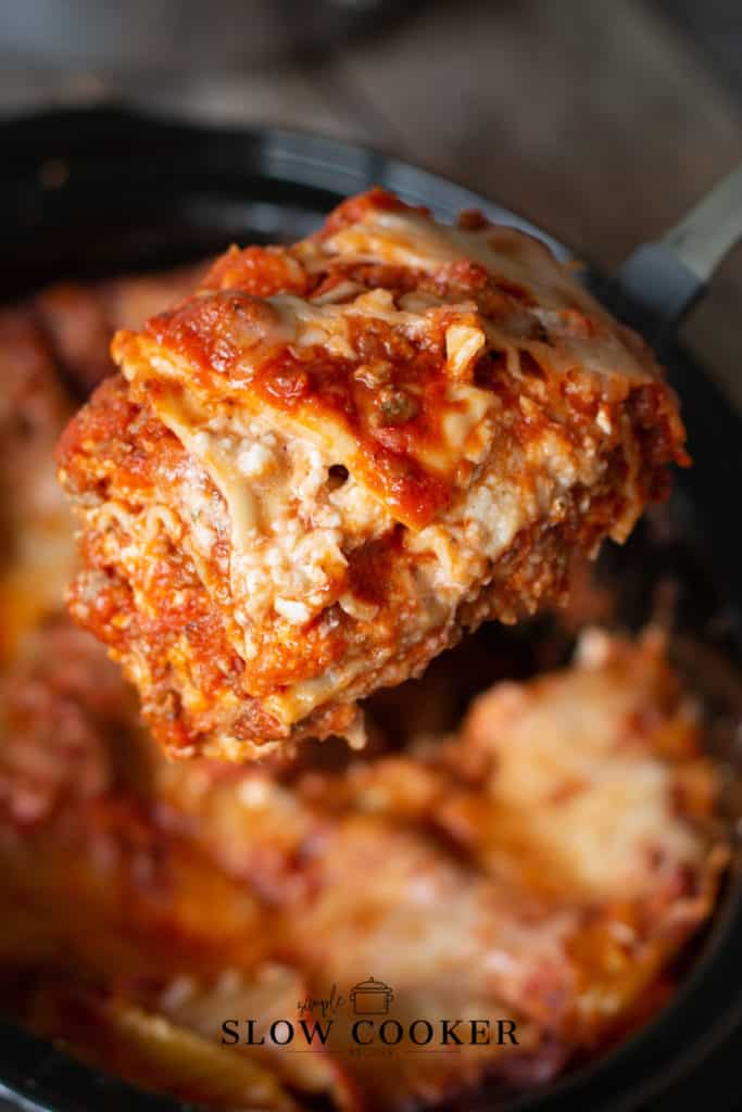 cut piece of slow cooker lasagna being lifted out of the black slow cooker.
