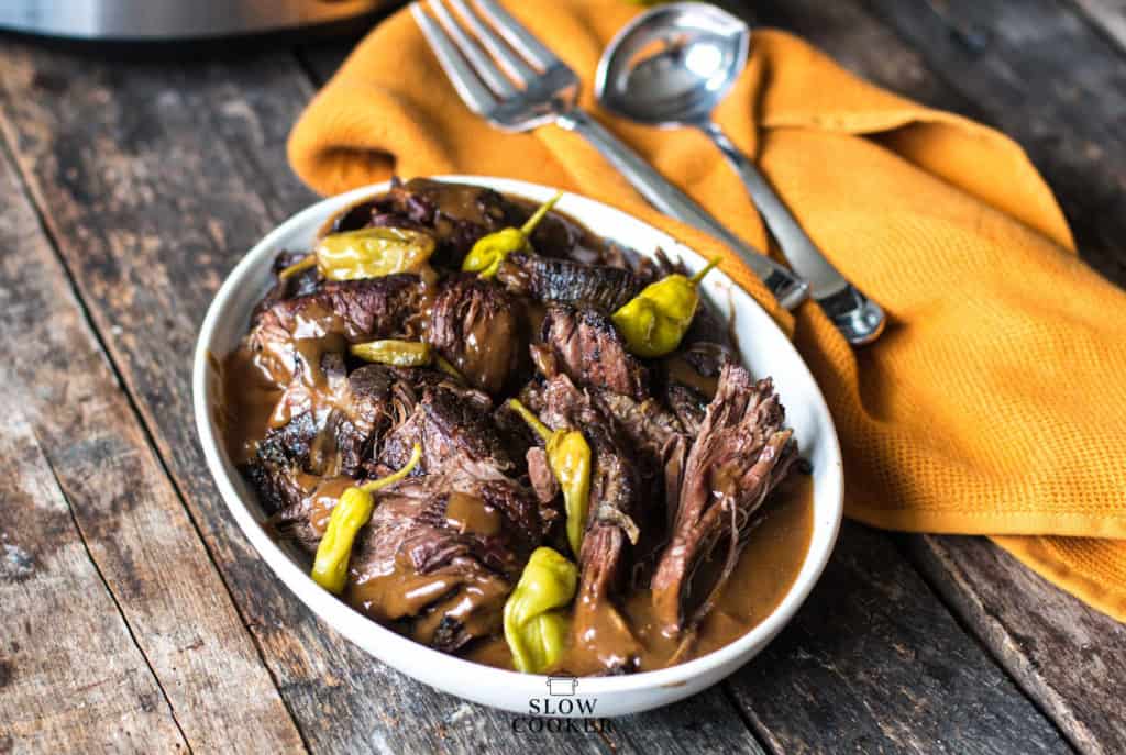 horizontal image of Slow Cooker Mississippi Pot Roast in a white oval dish with serving spoon and ladle off to the side.