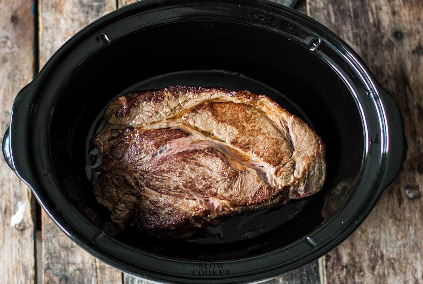 seared meat in the bottom of a slow cooker.