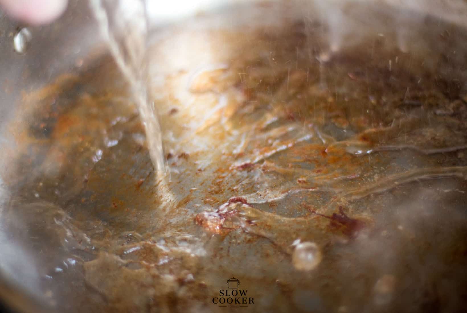 stock being poured into a hot pan to deglaze the pan.