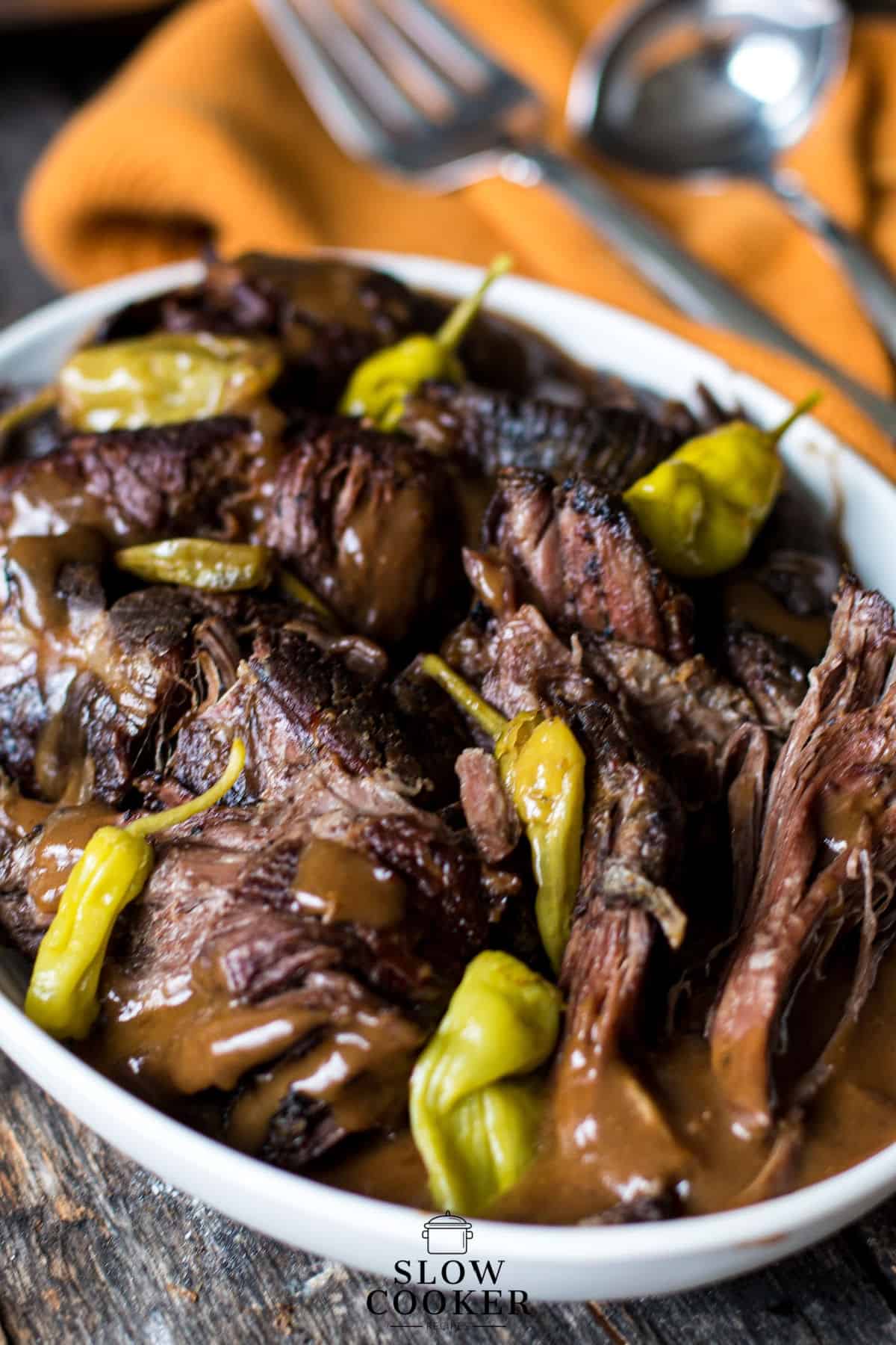 vertical image o Mississippi Pot Roast and gravy in a white bowl, orange towel in the background.