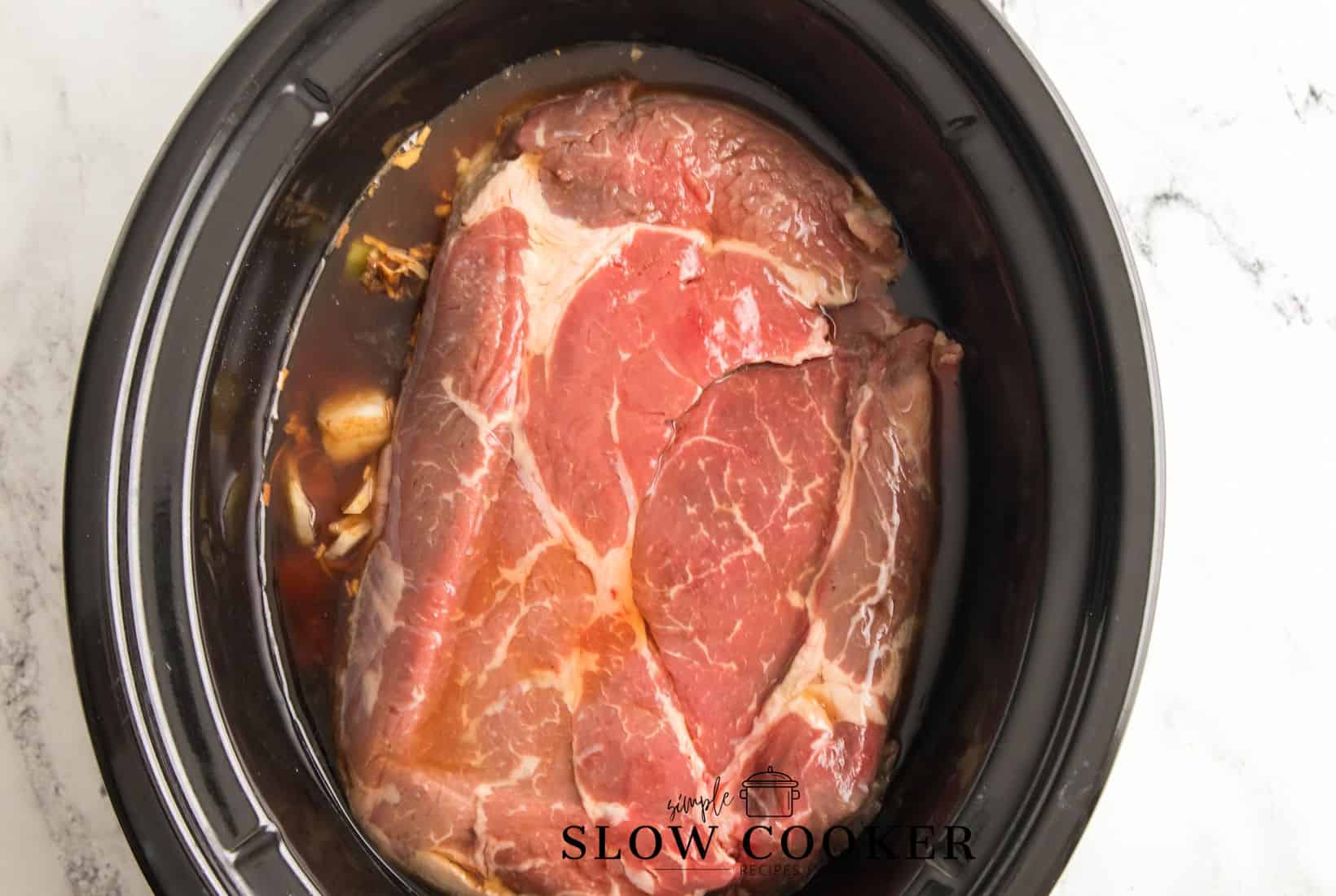 chuck roast added to the beer and broth covered veteables in a slow cooker.