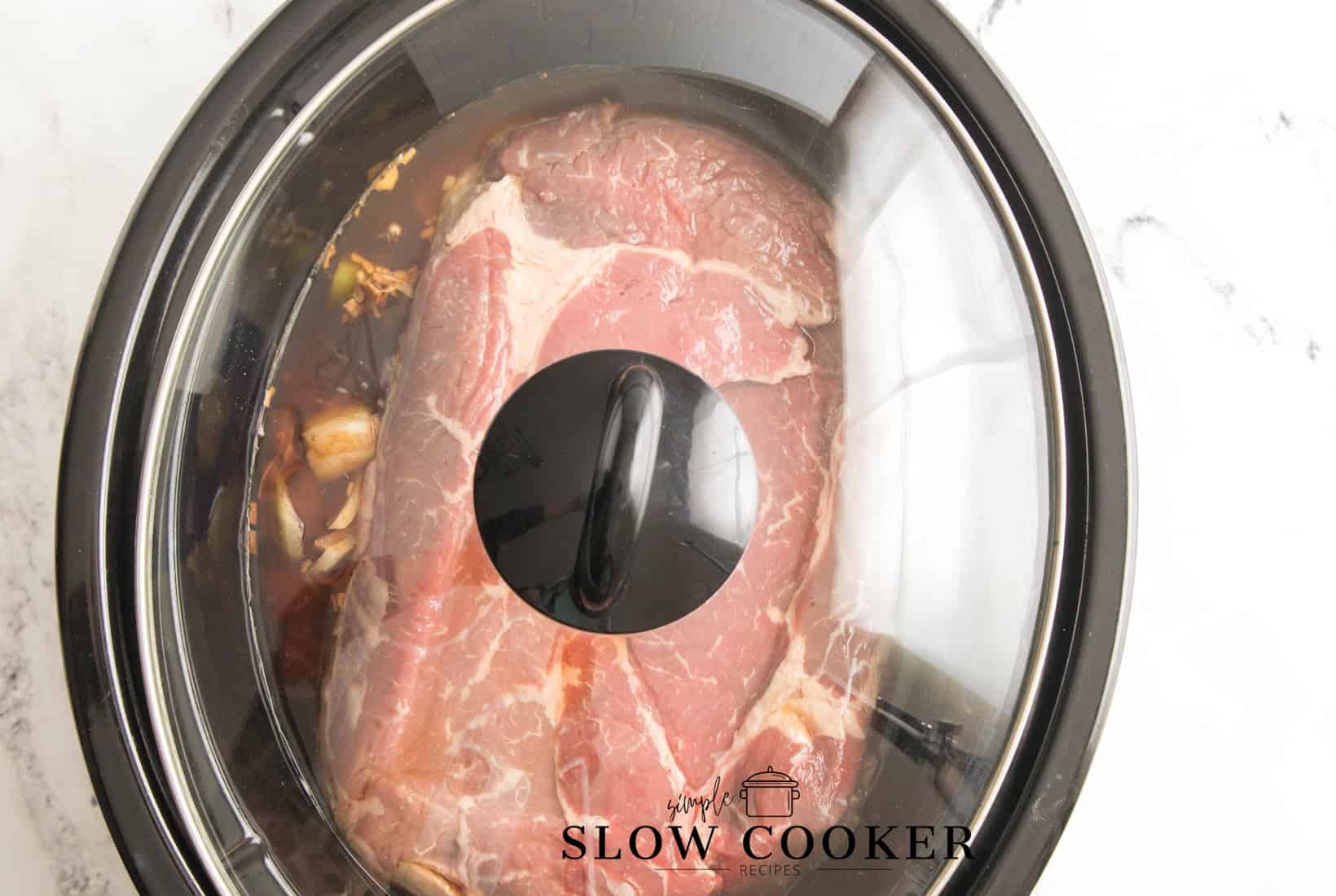 lid added to the slow cooker with pot roast ingriedints in the pt.