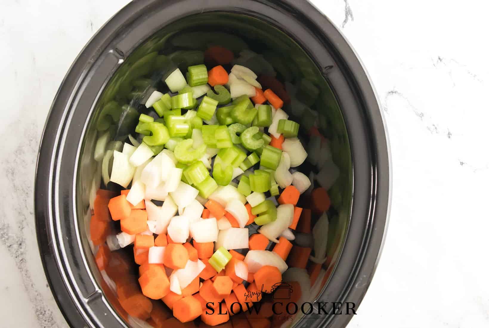 slow cooker with celery, onions and carrots in the bottom.