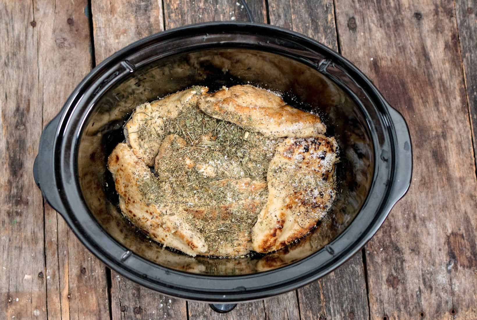 herbs added to chicken breasts in a slow cooker for Marry Me Chicken